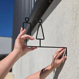 Matte black projecting toilet sign with male and female silhouettes against a concrete wall