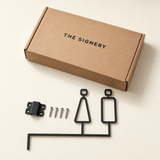 Matte black male and female toilet sign with mounting components and The Signery packaging