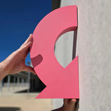 Vibrant pink fabricated curved arrow sign held against a concrete wall